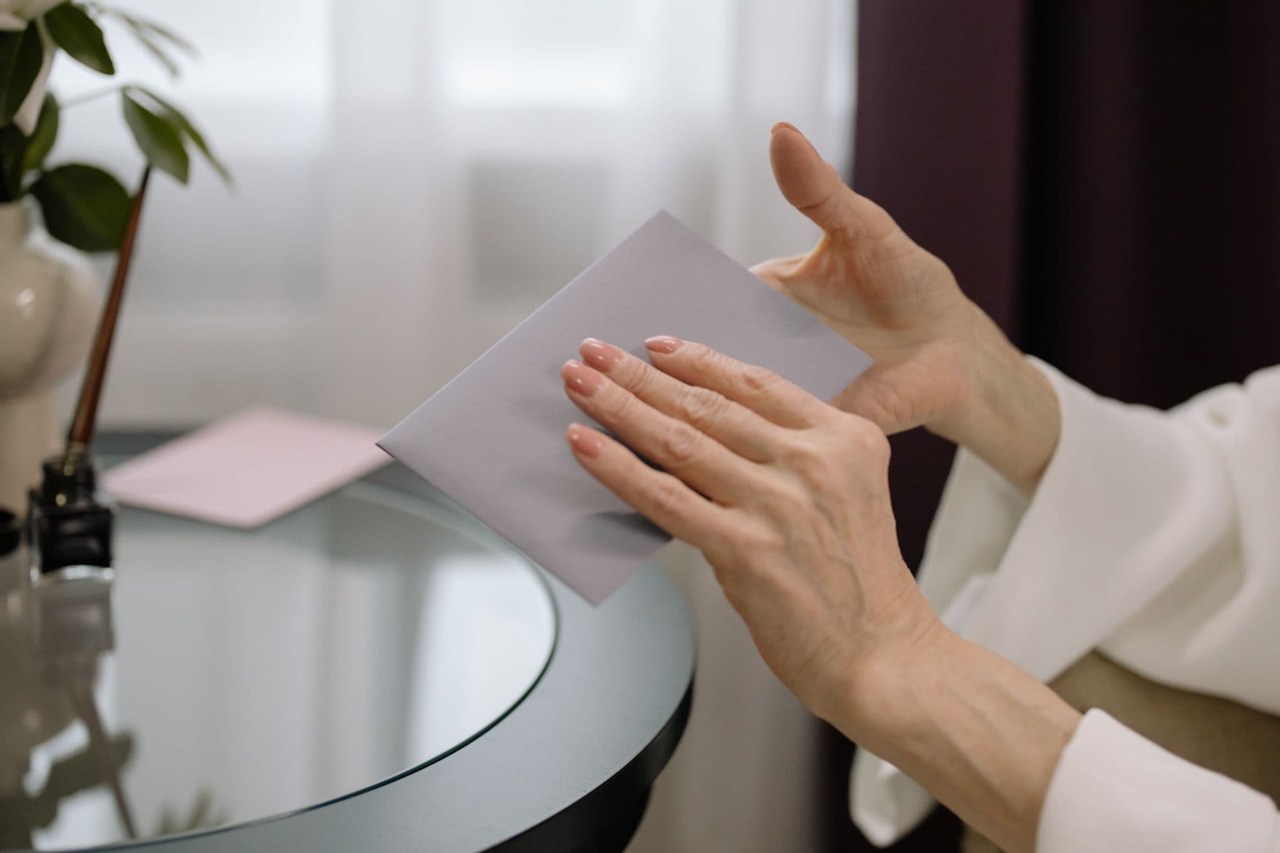 Two hands hold an unopened envelope at a table.
